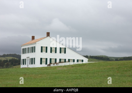La maison blanche James Johnston à Half Moon Bay présente des volets verts et un toit de boîte à sel, située sur une colline herbeuse sous un ciel gris nuageux. Banque D'Images