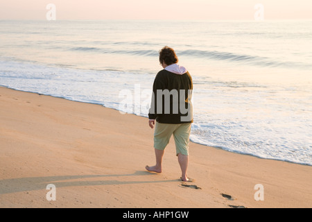 Une femme d'âge moyen de marcher dans le sable le long de la côte de l'océan au lever du soleil. Banque D'Images