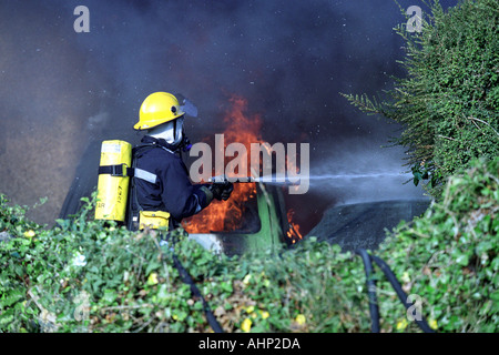 À l'aide d'un enrouleur de tuyau pompier jet d'éteindre un feu de voiture, la Grande-Bretagne UK Banque D'Images