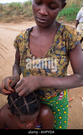 Coiffeur de bord de route braidant les cheveux d'une jeune femme au bord de la route. Mozambique Banque D'Images