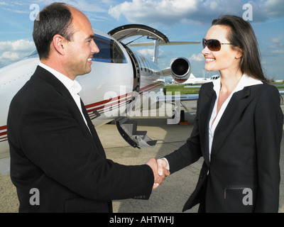 Businessman and businesswoman shaking hands en face de jet privé. Banque D'Images