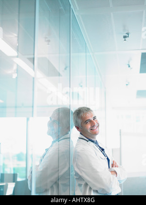 Smiling doctor leaning on mur en verre du hall de l'hôpital. Banque D'Images