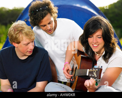 Deux jeunes hommes watching girl playing guitar Banque D'Images