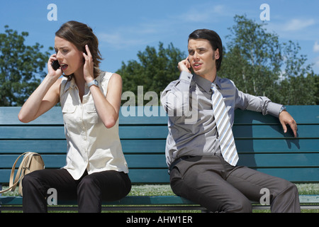 Les femmes d'affaires et de parler sur les téléphones portables en position assise sur un banc à l'extérieur. Banque D'Images