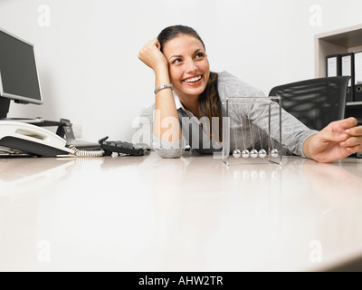 Businesswomen assise à son bureau avec un Newton's cradle Banque D'Images