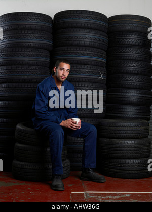 Mécanicien assis sur une pile de pneus Banque D'Images
