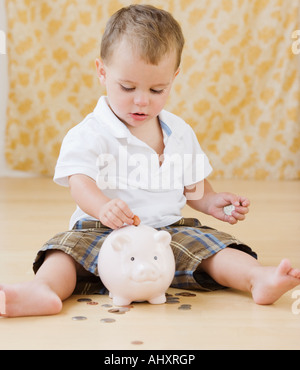 Baby putting coins in piggy bank Banque D'Images