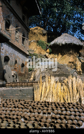 Poterie traditionnelle séchant au soleil à Pottery Square, Bhaktapur, Népal, avec des paquets de paille et d'anciens bâtiments en briques en arrière-plan. Banque D'Images