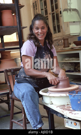 Happy woman sitting at a potters roue tourne un gros morceau d'argile et commence à créer un bol Banque D'Images