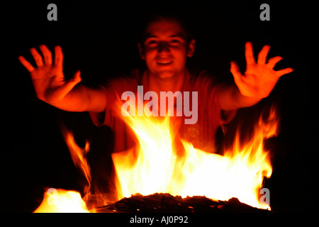 Jeune homme de se réchauffer par le feu de camp Photo de nuit portée de main pour les flammes Banque D'Images