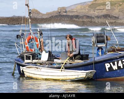 Cornish pêcheur dans son bateau de pêche avec un bateau à rames sur le côté de la marée Banque D'Images