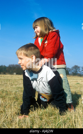 Petite fille assise sur son grand frère est de retour dans un champ Banque D'Images