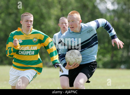 Action du joueur de football gaélique écolier exécutant avec la balle d'être poursuivi dans le comté d'Antrim en Irlande du Nord Belfast Banque D'Images