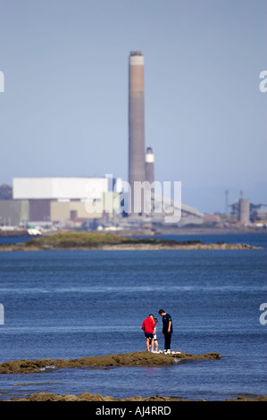 Les garçons jouent sur les roches par la mer en vue de kilroot power station jordanstown carrickfergus Belfast Lough en Irlande du Nord Banque D'Images