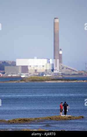 Les garçons jouent sur les roches par la mer en vue de kilroot power station jordanstown carrickfergus Belfast Lough en Irlande du Nord Banque D'Images