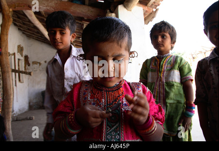 Jeune enfant tribal Harijan avec une oreille pleine de boucles d'oreilles jouant avec une cuillère à Bhirandiara Village, district de Kutch, Gujarat, Inde Banque D'Images