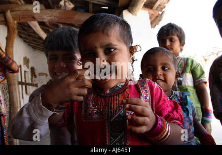 Jeune enfant tribal Harijan avec une oreille pleine de boucles d'oreilles mangeant de la cuillère à Bhirandiara Village, district de Kutch, Gujarat, Inde Banque D'Images