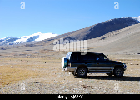 Les cimes enneigées du haut de l'Himalaya au Tibet sont vus au-dessus des collines arides du plateau tibétain avec un Landcruiser touristiques Banque D'Images