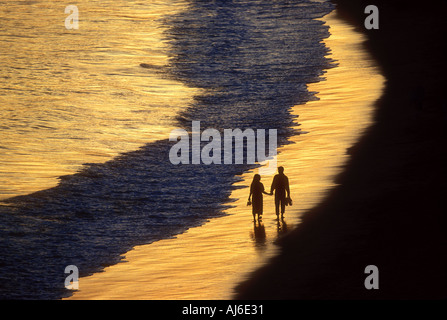 Couple en train de marcher le long de la plage au coucher du soleil près de l'eau Parution du modèle de droit Banque D'Images