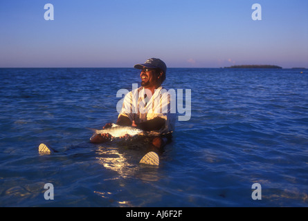 Homme assis dans l'eau peu profonde holding bonefish pris alors que la pêche à la mouche au Belize Caraïbes Parution Modèle droit Banque D'Images