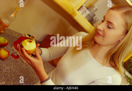 Young woman peeling une pomme dans la cuisine. Banque D'Images