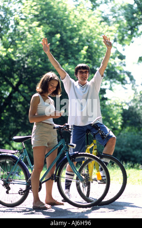 Jeune couple riding a vélos dans le parc et parler dans les téléphones mobiles. Banque D'Images