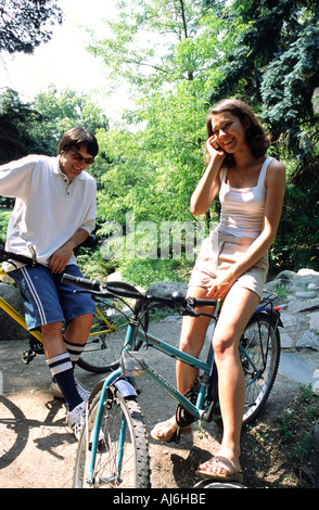 Jeune couple riding a vélos dans le parc et parler dans les téléphones mobiles. Banque D'Images