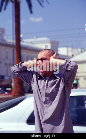 Jeune homme couvrant ses oreilles et crier sur une rue animée. Banque D'Images