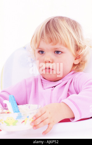 Tout-petit enfant 0 5 peau claire dodus juste juste aux cheveux bouclés blonds babygro s'asseoir manger des aliments table Banque D'Images