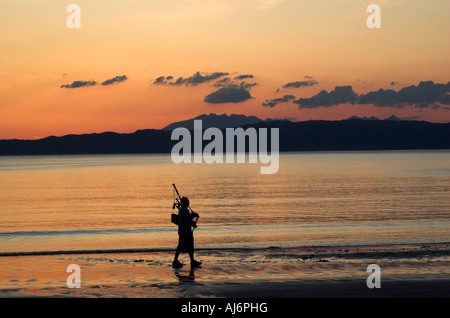 Un joueur de cornemuse silhouette sur le coucher du soleil sur la plage d'Arisaig dans les highlands avec Skye au-delà Banque D'Images