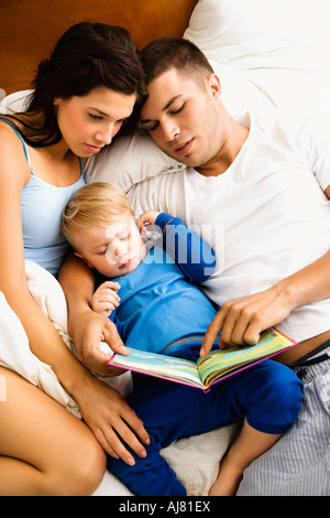 Les parents de race blanche et petit garçon reading book in bed Banque D'Images
