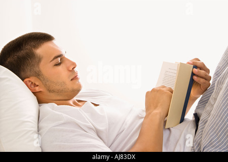 Vue latérale du beau portrait of mid adult man Lying in Bed reading a book Banque D'Images