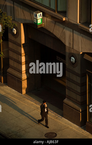 Man with coffee cup promenades dans la lumière du soleil tôt le matin sur le trottoir près de l'arrêt de métro sur la 48e rue à Manhattan, nouveau Banque D'Images