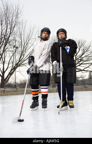 Deux garçons en hockey sur glace uniforms holding des bâtons de hockey sur glace en patins à glace Banque D'Images