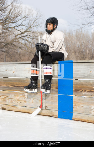 Garçon en uniforme de hockey bâton de hockey maintenant assis sur de touche Banque D'Images