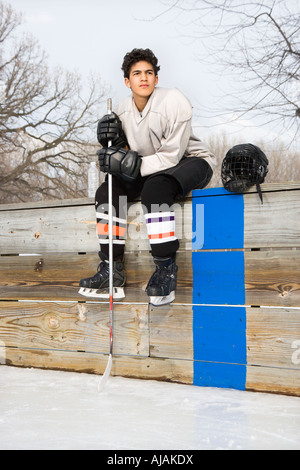 Garçon en uniforme de hockey bâton de hockey maintenant assis sur de touche Banque D'Images