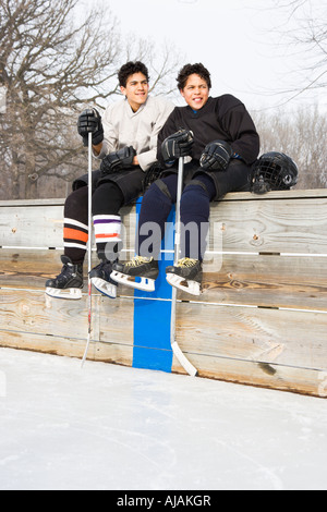 Deux garçons en uniforme de hockey sur glace assis sur de touche à la patinoire et souriant Banque D'Images