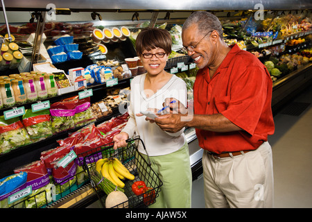 Middle aged African American man and woman in grocery store souriant et pointant sur la liste d'achats Banque D'Images