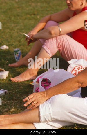 Deux femmes s'asseoir dans un espace vert public à fumer leurs cigarettes lors d'un festival annuel de musique dans un parc du sud de Londres Banque D'Images
