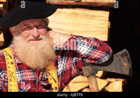 Agriculteur barbu assis en face de pile de bois, portant béret, s'appuyant sur ax Banque D'Images