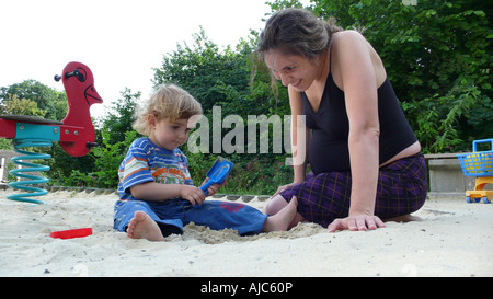 Mère enceinte avec son petit garçon dans un bac à sable, Allemagne Banque D'Images