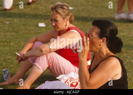 Deux femmes s'asseoir dans un espace vert public à fumer leurs cigarettes lors d'un festival annuel de musique dans un parc du sud de Londres Banque D'Images