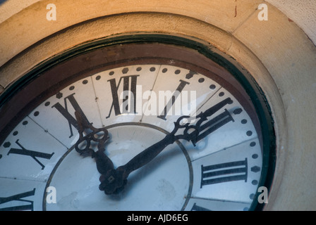 Une vieille horloge murale analogique avec chiffres romains dans les heures, iluminated sur le coucher du soleil. Banque D'Images