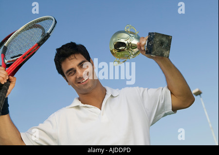 Joueur de tennis masculin soulevant des raquettes de tennis et le trophée, portrait Banque D'Images