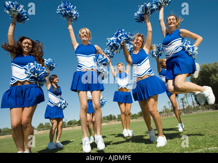 Groupe de cheerleaders rising pom-poms, sautant sur terrain de football Banque D'Images