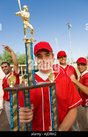 Baseball player holding trophy sur champ, coéquipiers en arrière-plan Banque D'Images