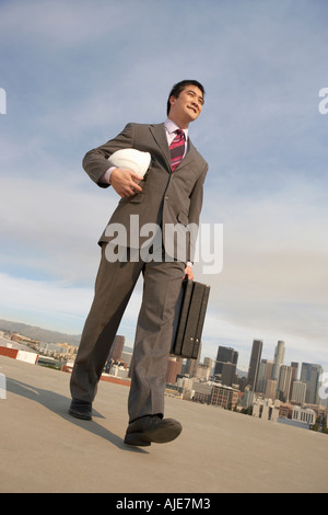 Business man carrying hard hat on city rooftop Banque D'Images