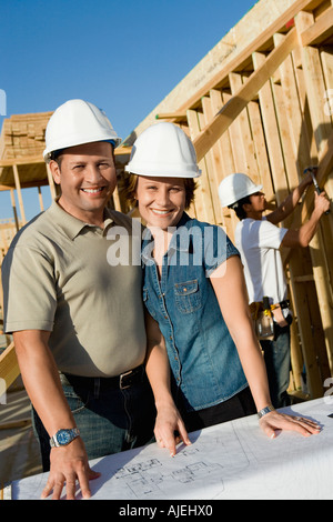 En couple avec des casques de plan directeur pour la construction d'une maison site, portrait Banque D'Images