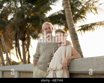 Senior couple leaning against wall, palmiers en arrière-plan Banque D'Images