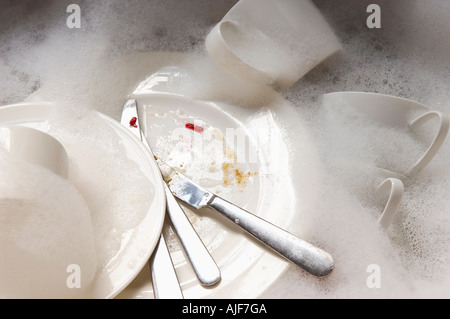 Pile de vaisselle sale et de l'argenterie dans le lavabo avec bulles, close-up Banque D'Images